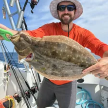 Man in orange shirt on boat holding a flounder.