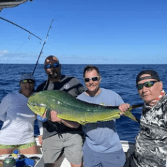 Four people on a boat holding a large fish against a backdrop of ocean and blue sky.