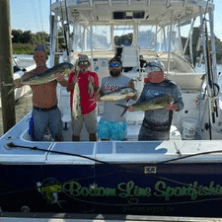 Four people on a boat holding large fish they caught.